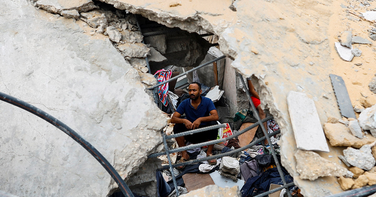 Un palestinese seduto tra le rovine di un palazzo bombardato. Foto: Reuters